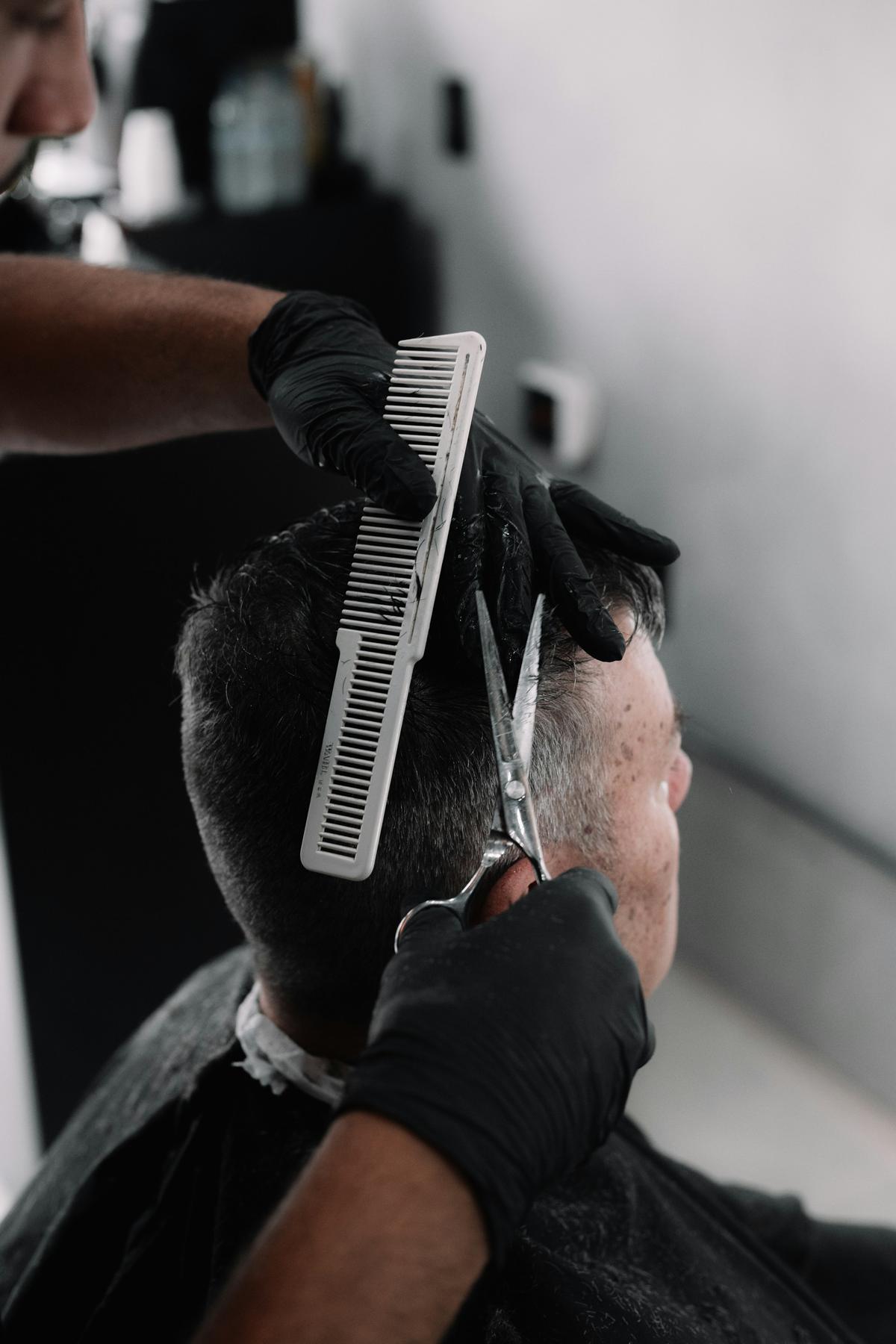 Barbier met zwarte handschoenen knipt met kam en schaar